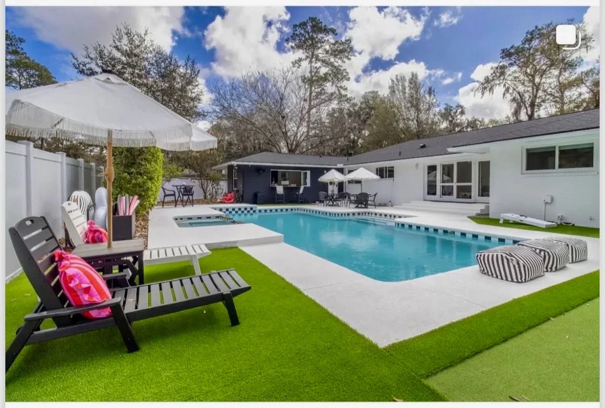 Turquoise pool with white concrete deck, artificial grass, and modern home