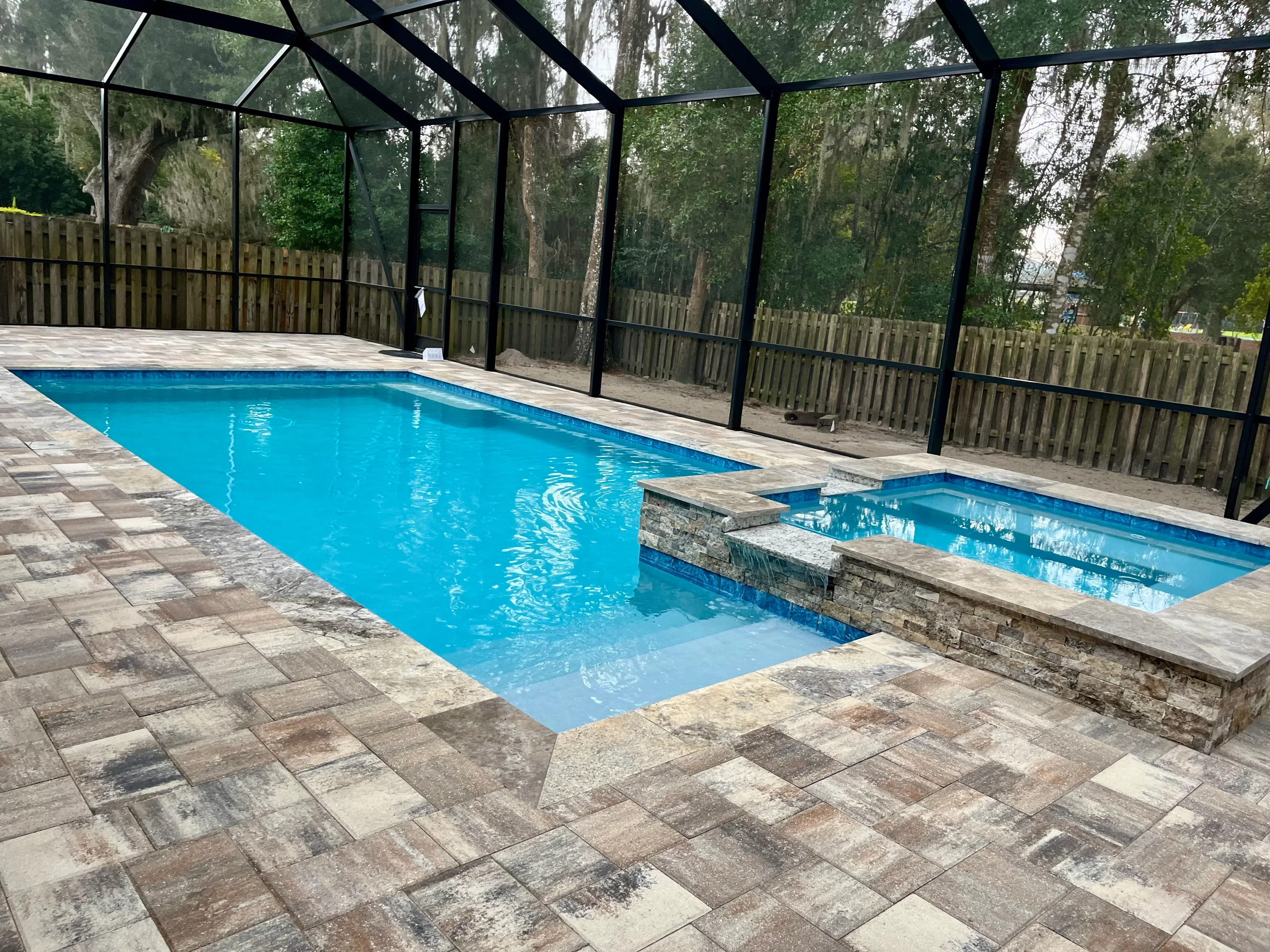 Rectangular pool with spa and black screen enclosure on paver deck