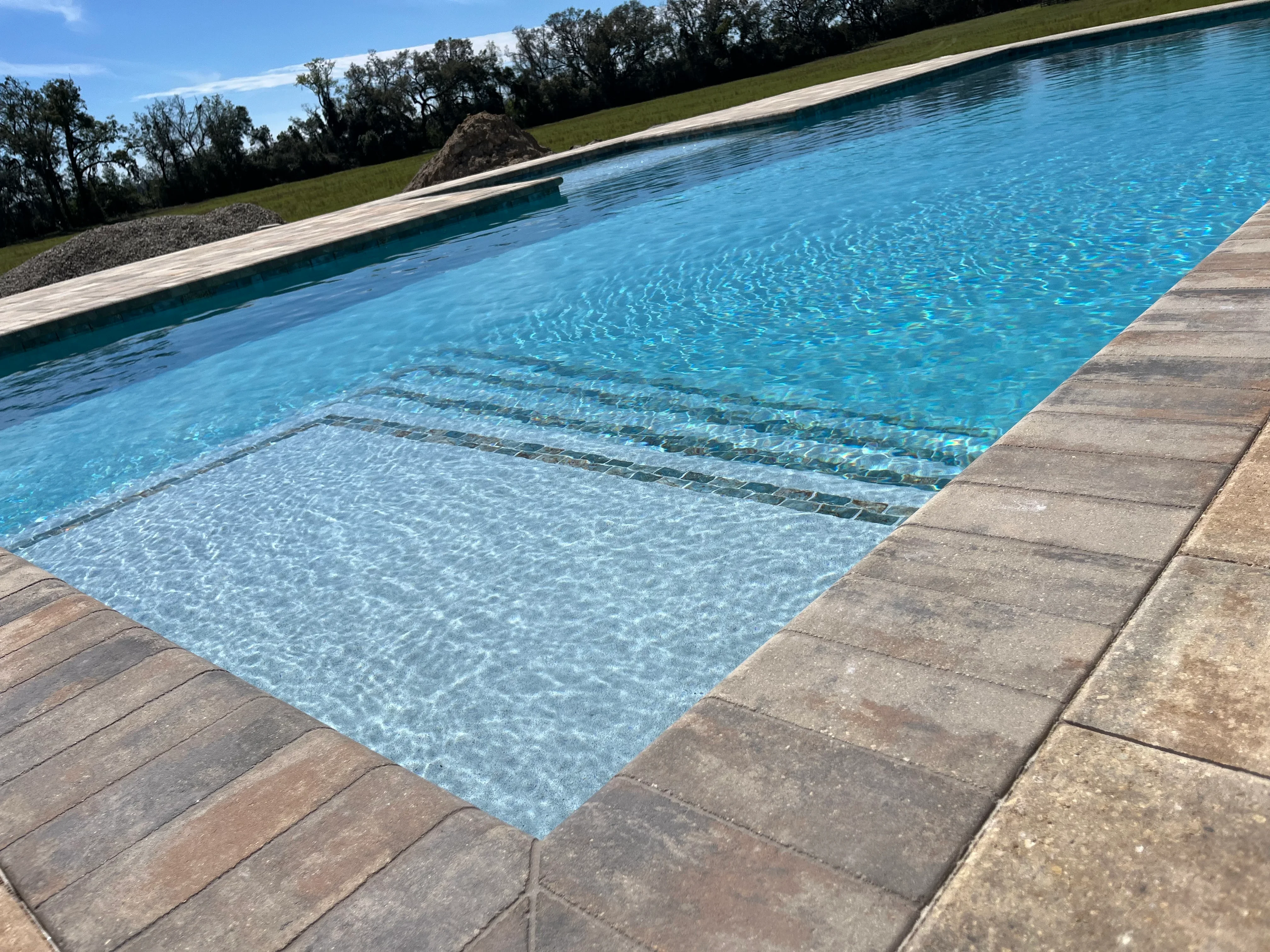 Rectangular swimming pool with composite decking and lush green lawn backdrop