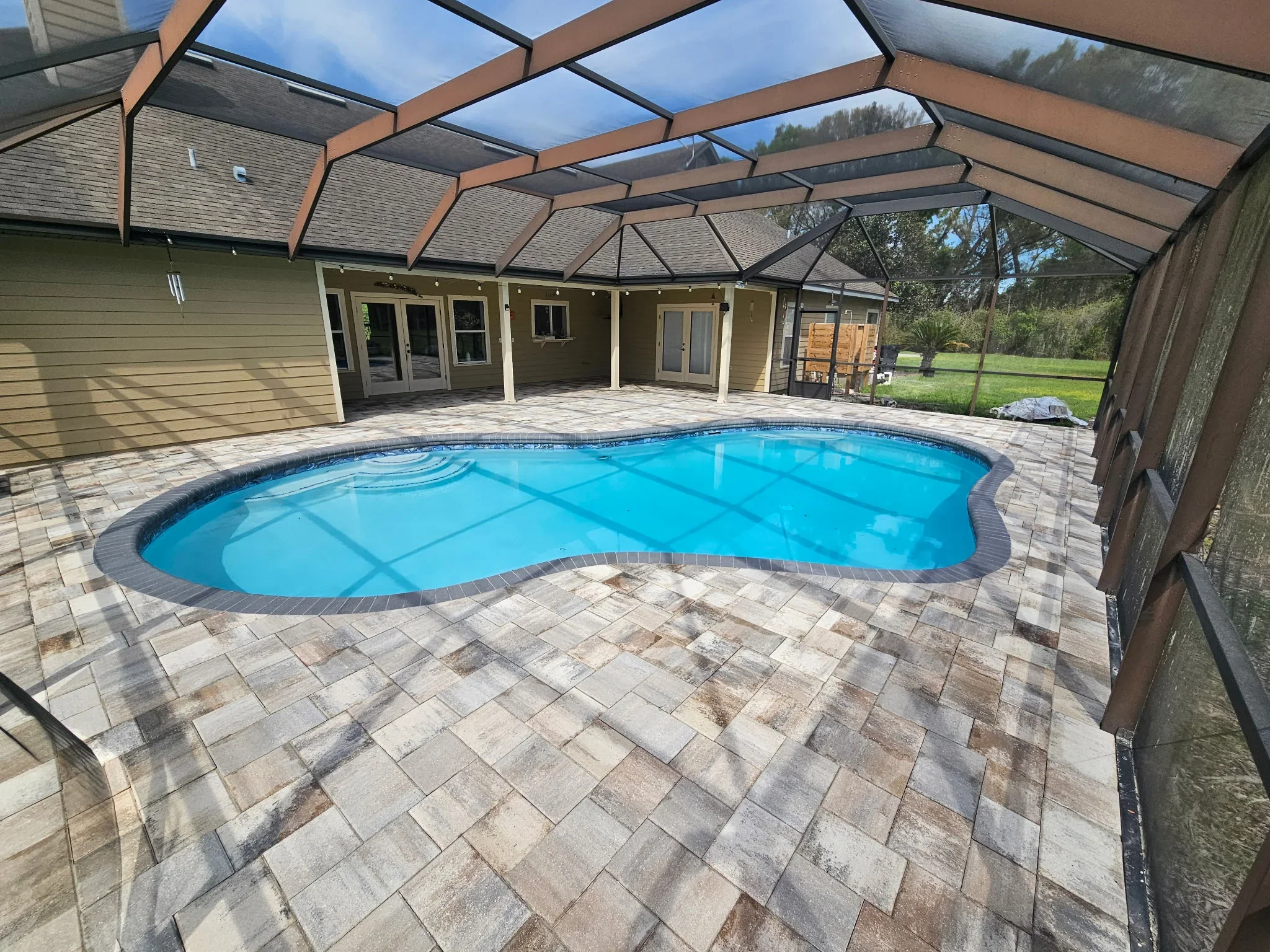 Freeform pool with screened enclosure and paver deck overlooking landscaped yard