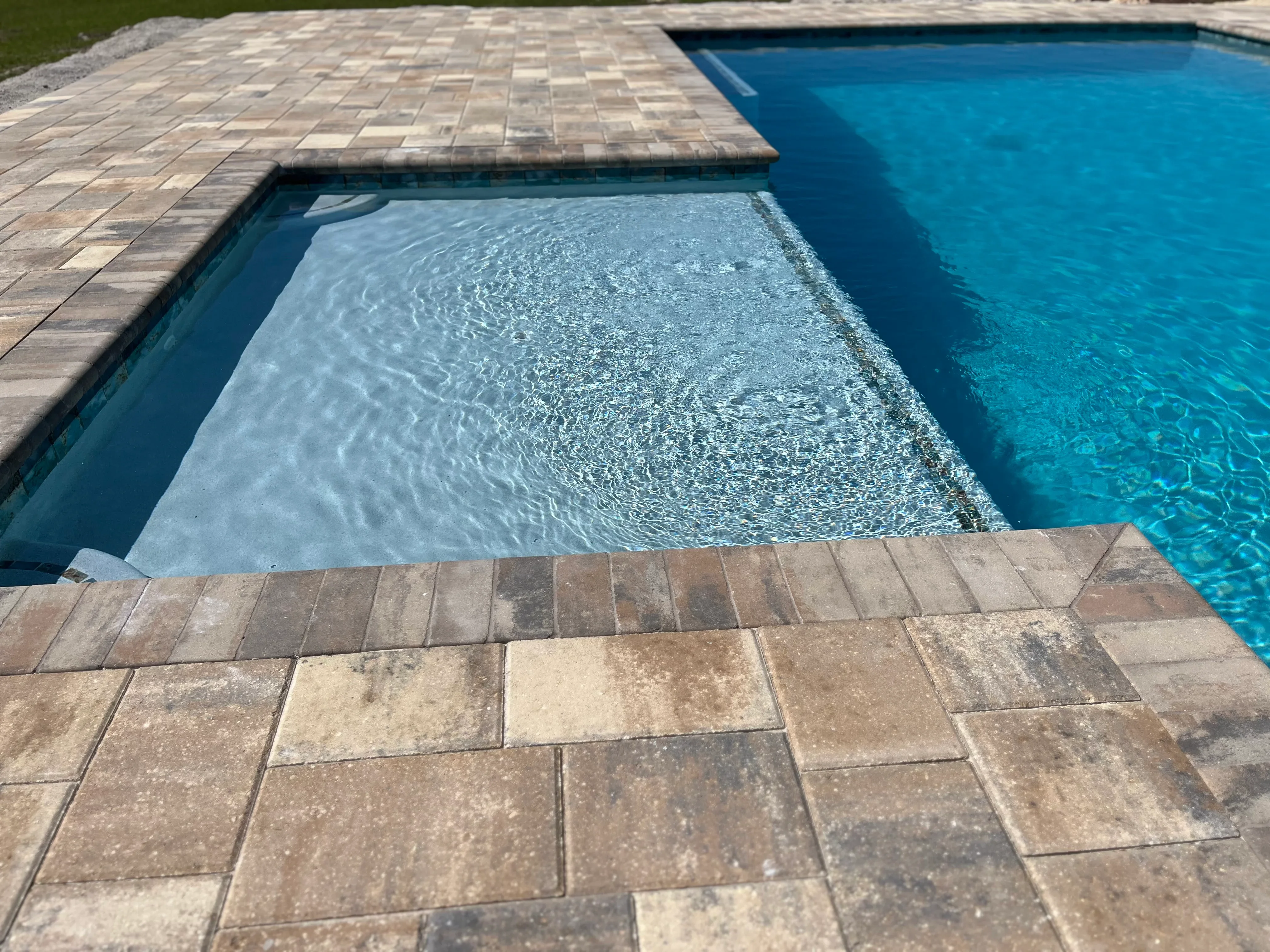 Custom pool with spa and tan paver deck overlooking crystal-clear blue water