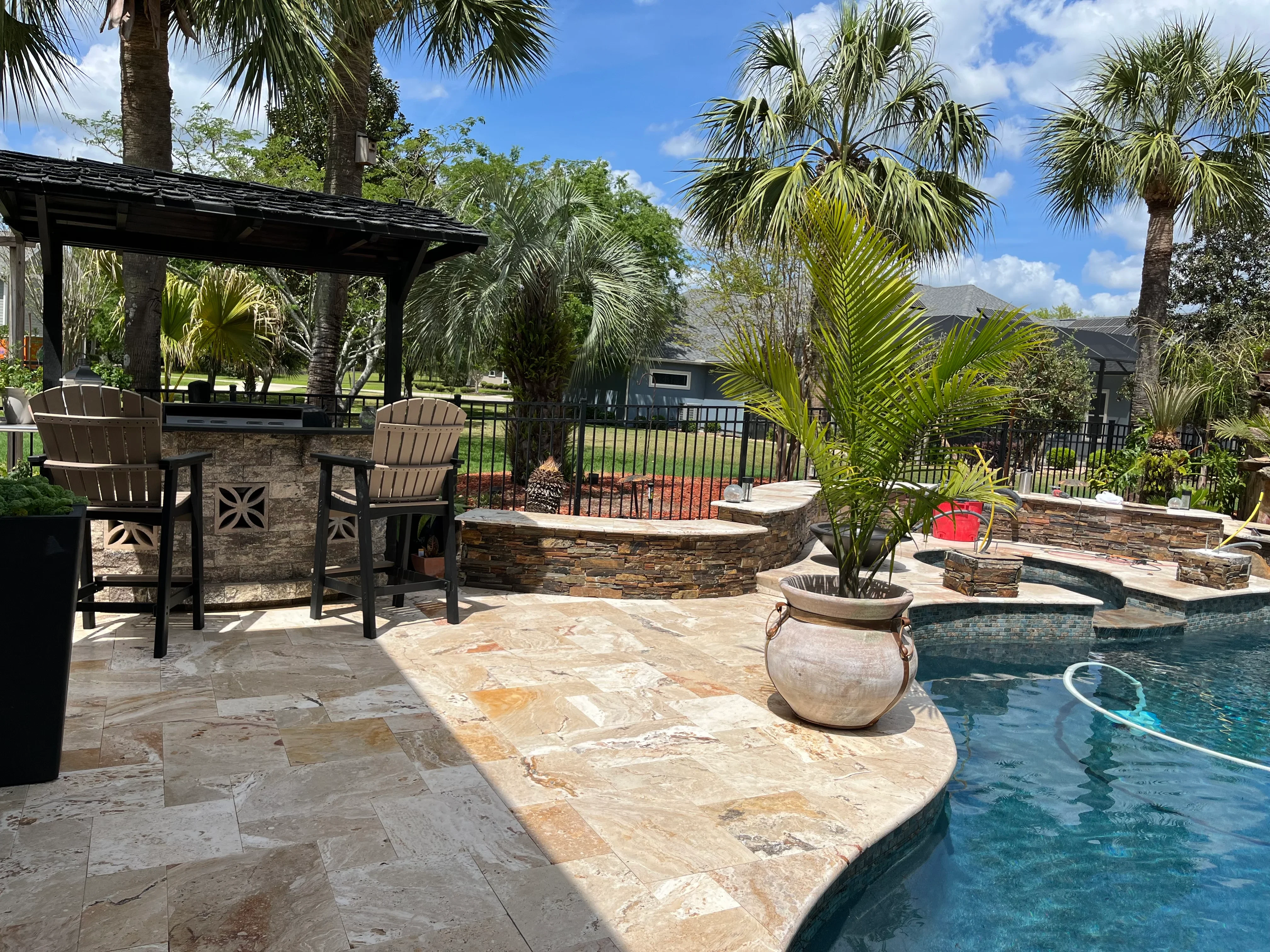 Luxury backyard pool with stone patio, pergola, and tropical landscaping in Alachua