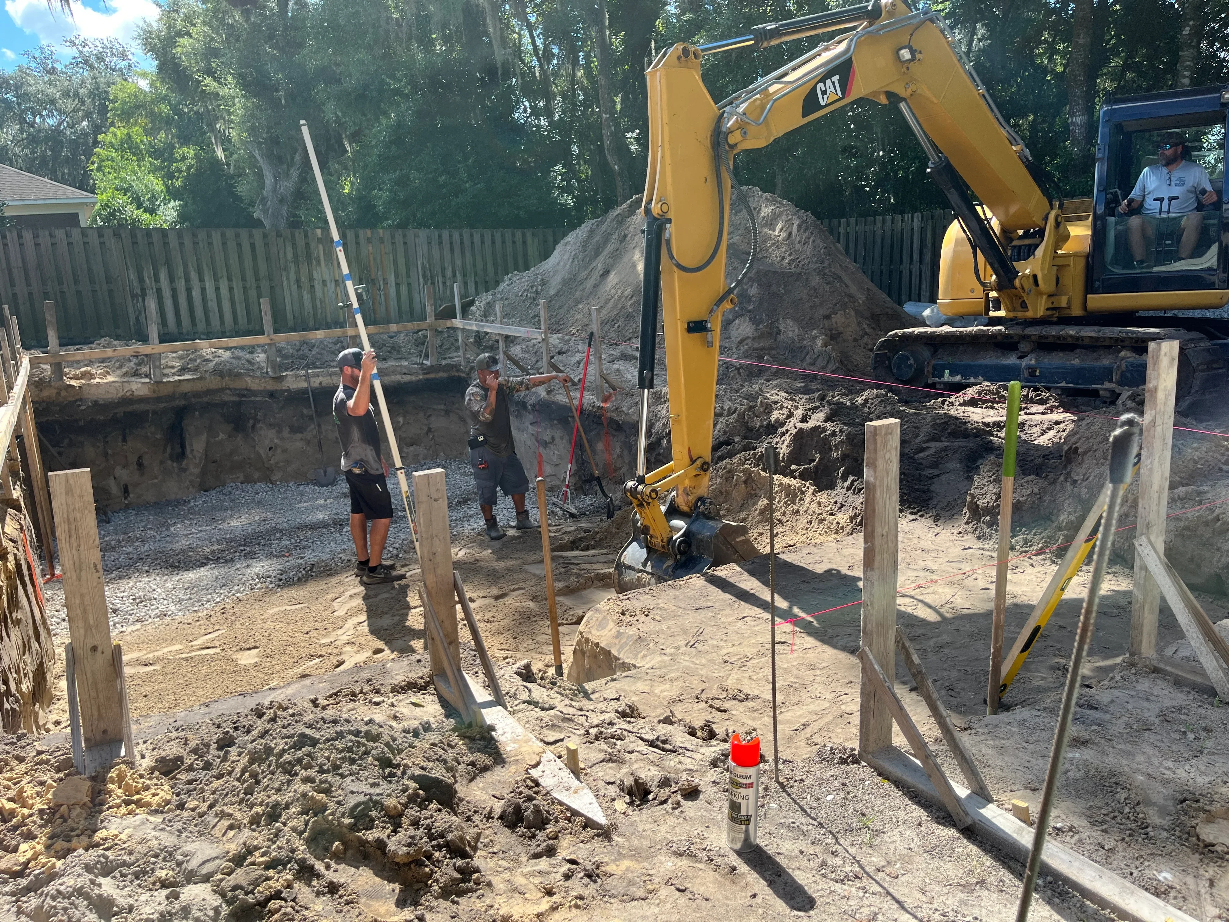 CAT excavator digging pool foundation with crew and wooden forms on residential property