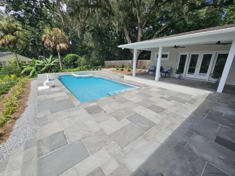 Rectangular pool with gray paver patio and white pergola structure in residential backyard