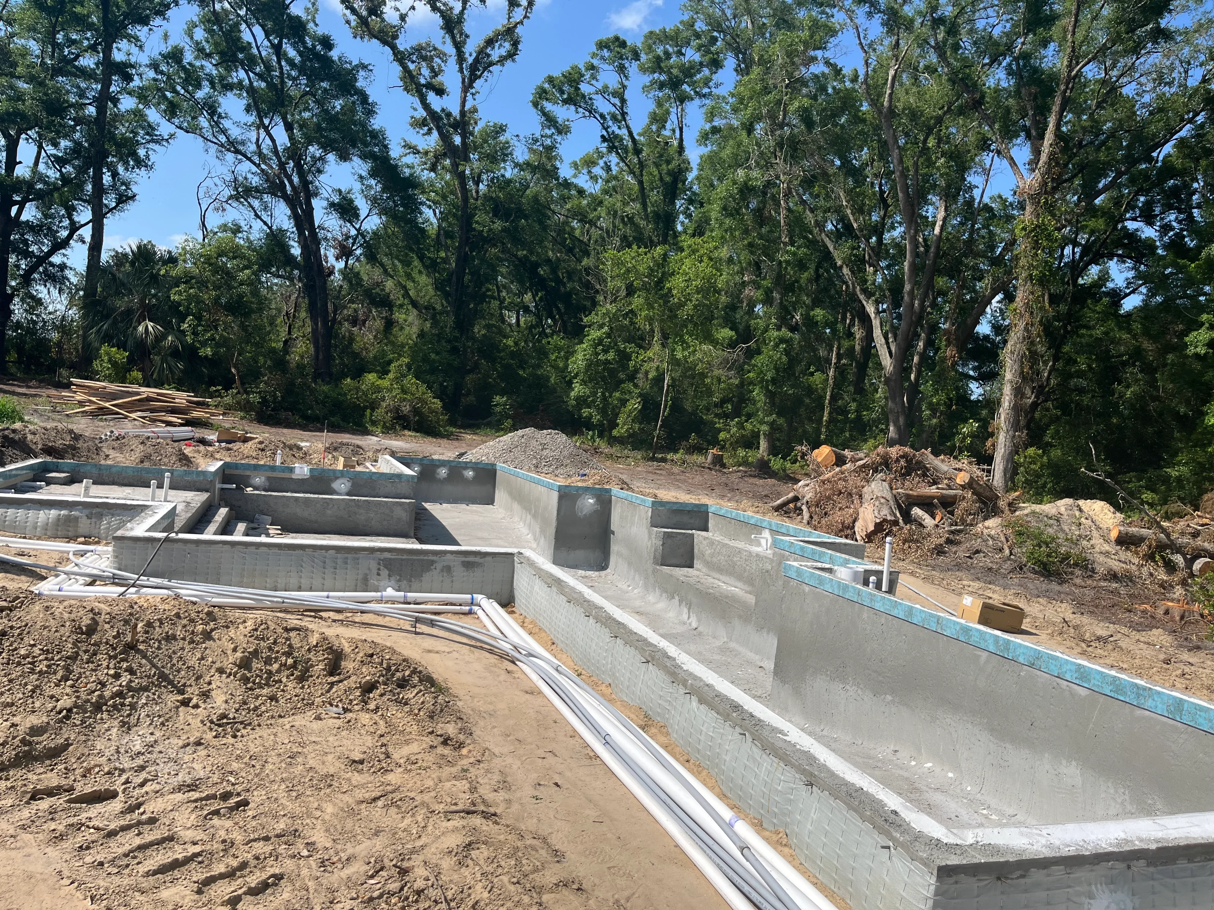 Concrete pool shell under construction with blue waterproofing membrane and formed walls